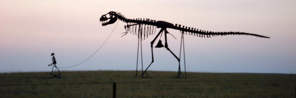 Statue of human skeleton with a T. Rex skeleton on a leash.